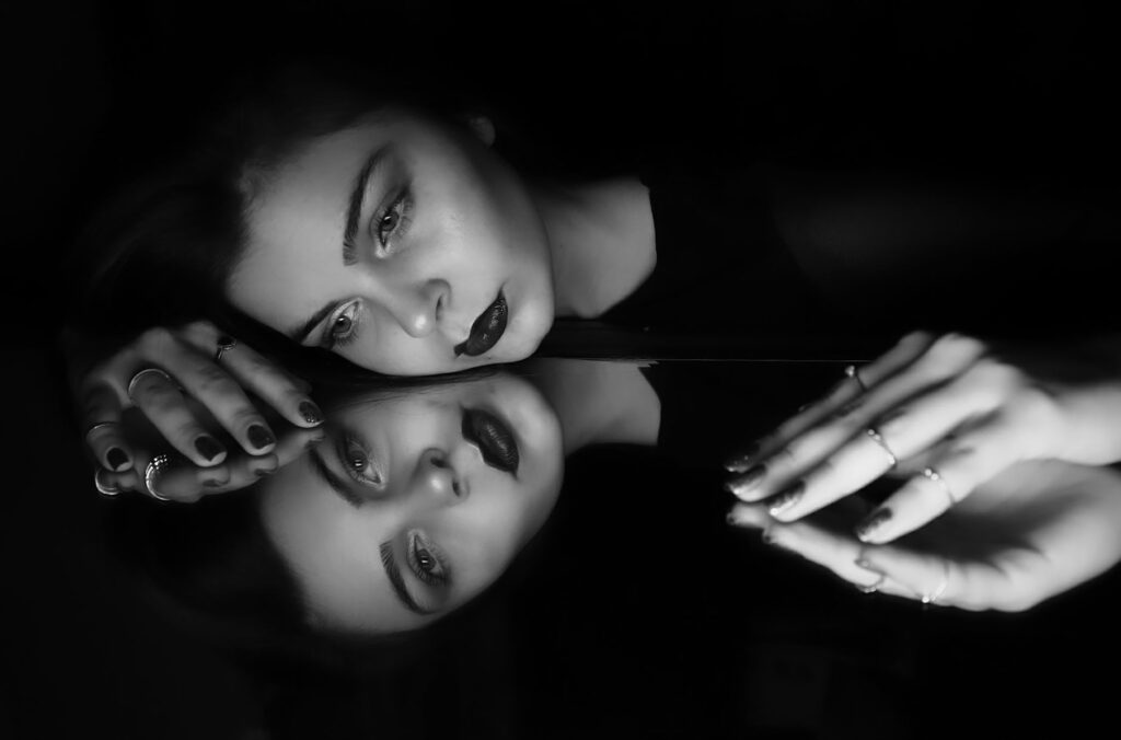 A striking black and white portrait of a woman contemplating her reflection in a mirror.