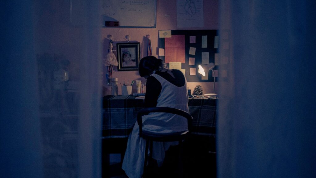 Woman in a white dress sitting at a desk in a dimly lit room, creating a romantic ambiance.