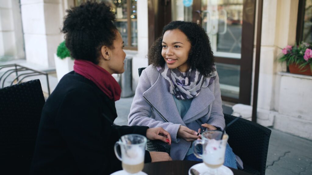 Two women having a warm conversation over coffee at an outdoor café setting.