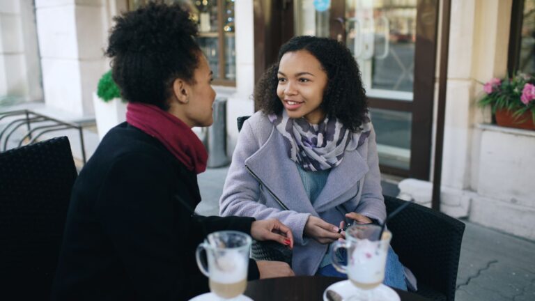 Two women having a warm conversation over coffee at an outdoor café setting.