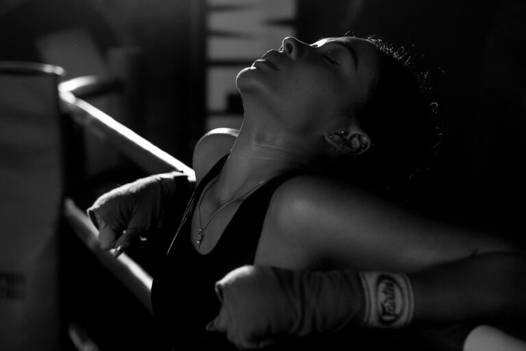 Black and white image of a tired female boxer taking a break in the ring.