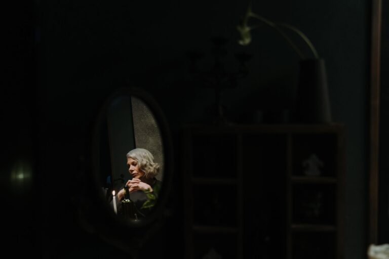 A senior woman is reflected in a mirror by candlelight, evoking introspection.