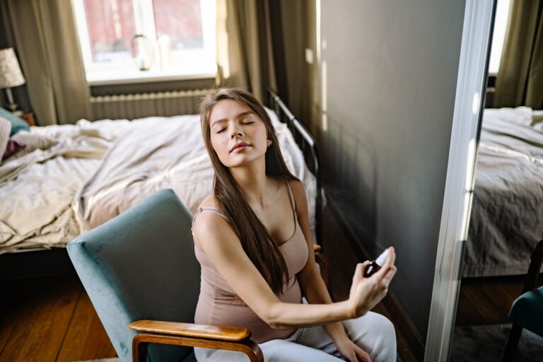 Pregnant woman sitting indoors, eyes closed, enjoying a refreshing fragrance.