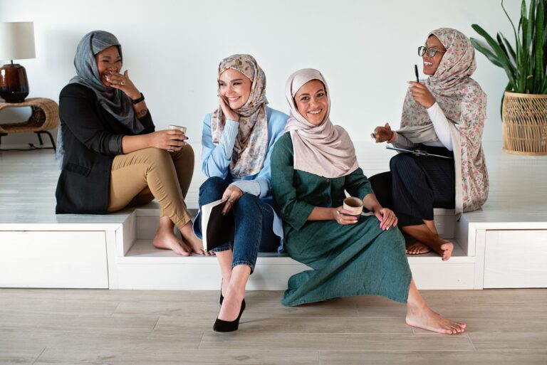 A group of diverse women in hijabs collaborate and enjoy coffee in a modern office.